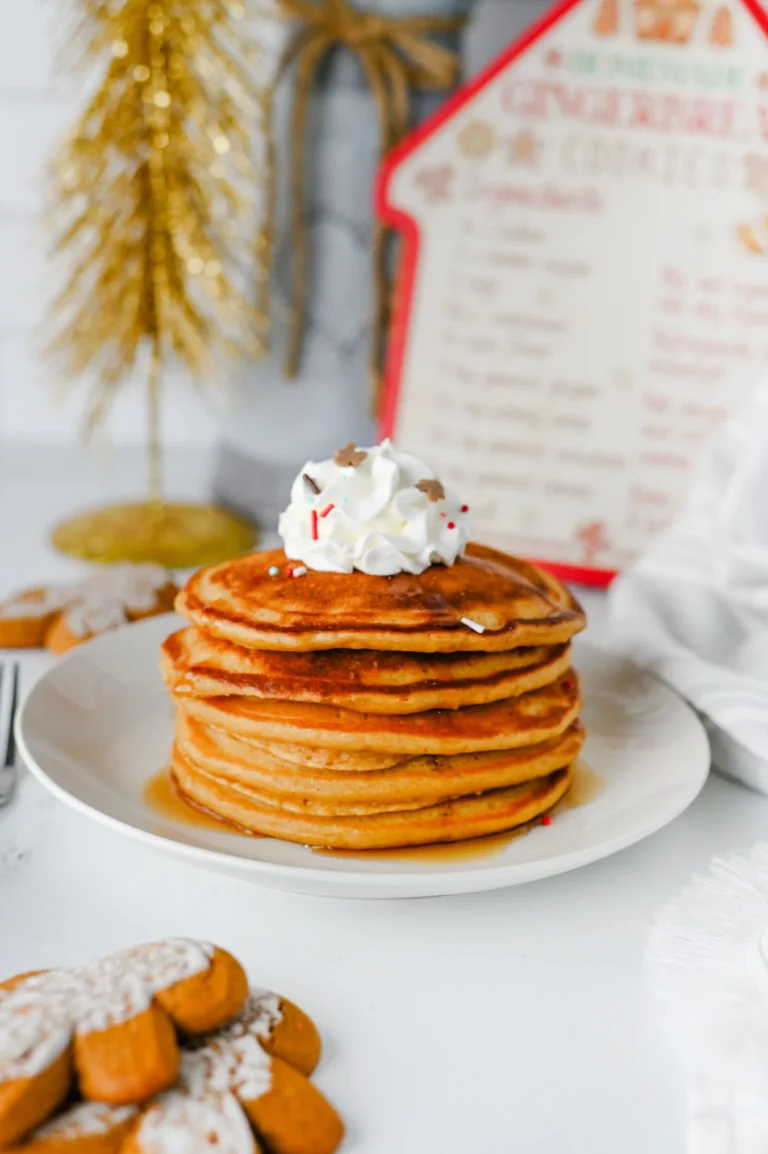 gingerbread pancakes stacked on a white plate with whipped cream on top