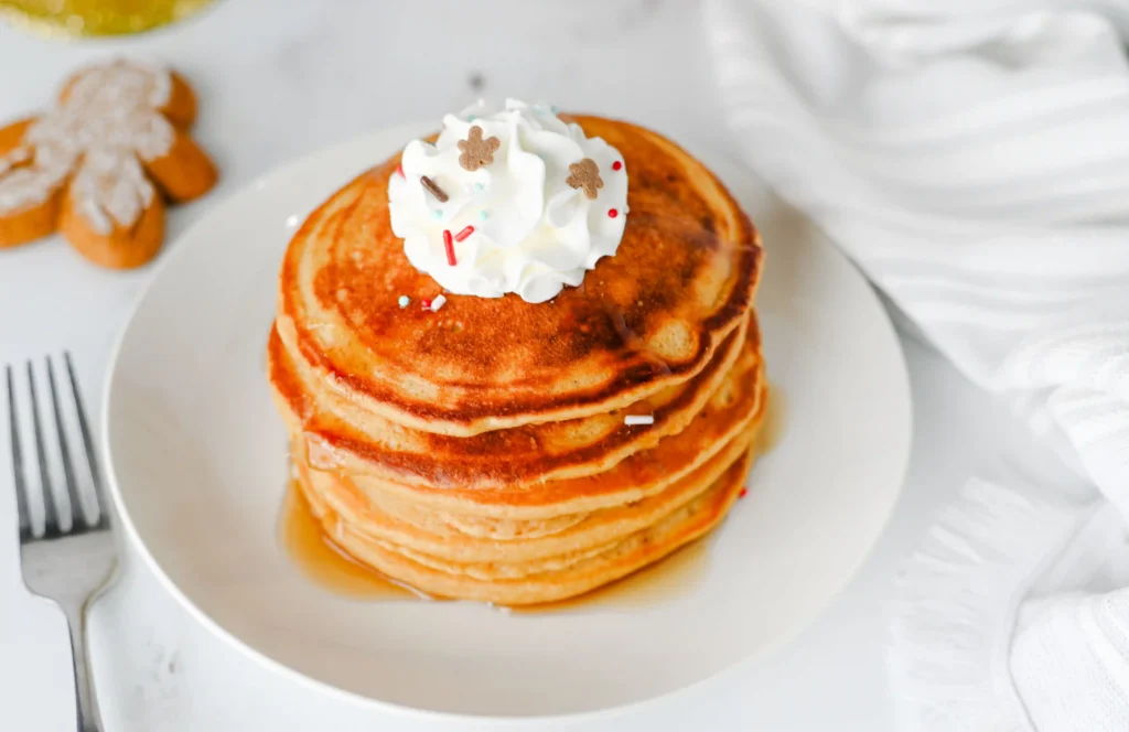 gingerbread pancakes stacked on a white plate with whipped cream on top
