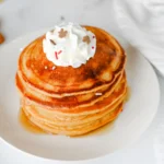 gingerbread pancakes stacked on a white plate with whipped cream on top