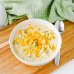Slow Cooker Broccoli Cheddar Soup with cheese in a white bowl on a wooden board