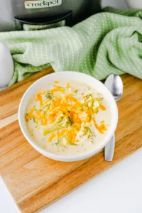 Slow Cooker Broccoli Cheddar Soup with cheese in a white bowl on a wooden board