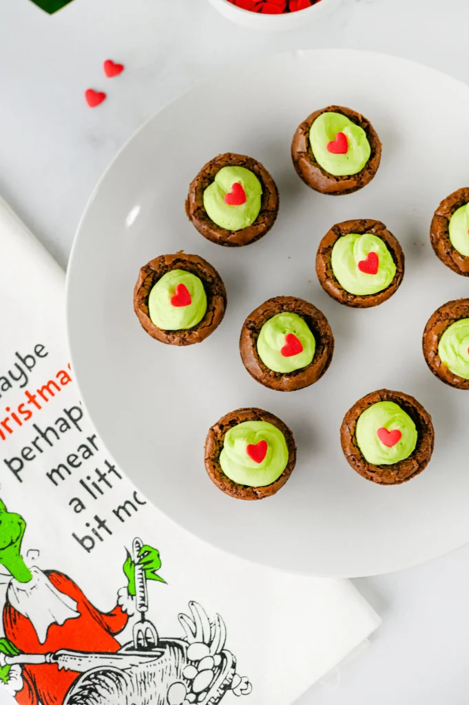 brownie bites with green frosting and a heart sprinkle on a white plate
