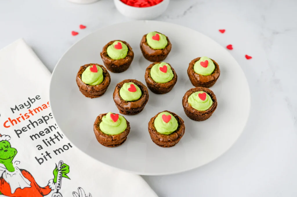 brownie bites with green frosting and a heart sprinkle on a white plate