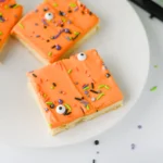 Halloween Sugar Cookie Bars with orange icing and halloween sprinkles