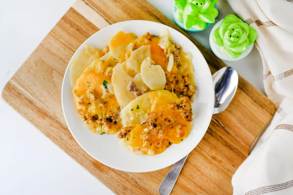 Hamburger Potato Casserole on a white plate resting on a wooden board with a spoon