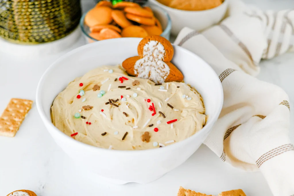Gingerbread dip with sprinkles in a white bowl with a gingerbread cookie in it