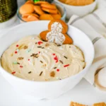 Gingerbread dip with sprinkles in a white bowl with a gingerbread cookie in it