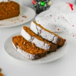 slices of a gingerbread loaf topped with powdered sugar on a white plate.