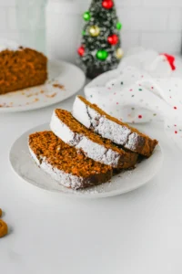slices of a gingerbread loaf topped with powdered sugar on a white plate.