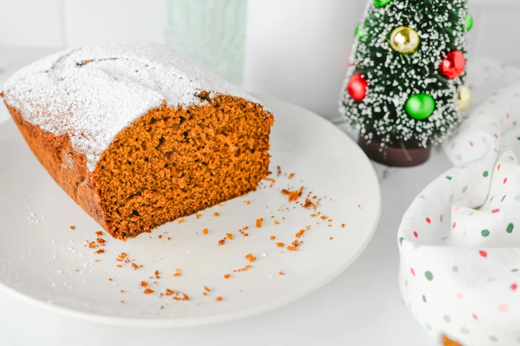 a gingerbread loaf topped with powdered sugar on a white plate.
