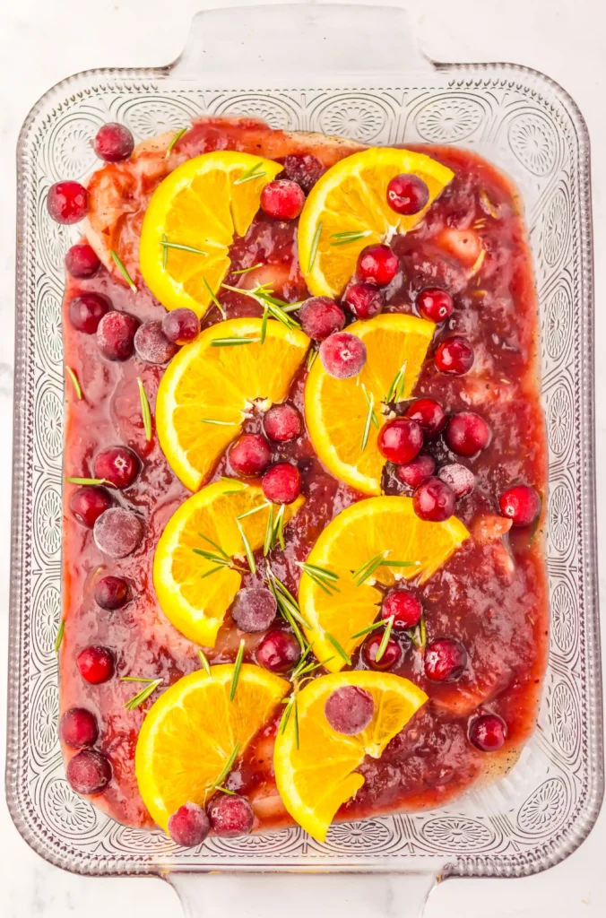 a baking dish with cranberry sauce, chicken, and orange slices