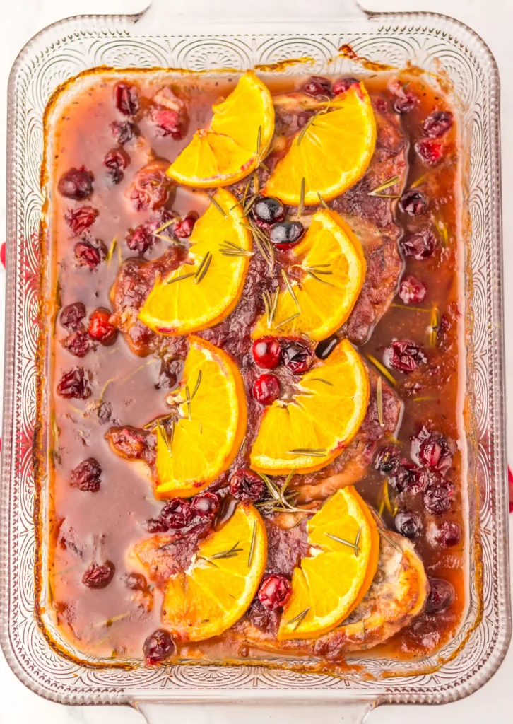 a baking dish with cranberry sauce, chicken, and orange slices