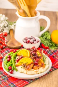baked Christmas chicken with cranberries and lemon slices on a plate with green beans