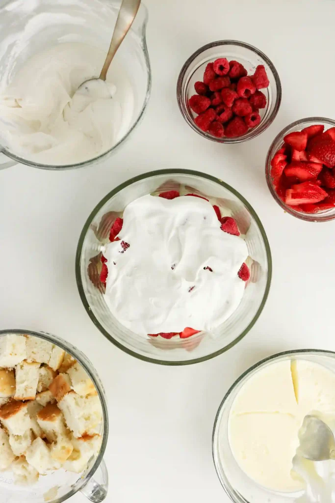cake cubes, pudding mix, and strawberries in a trifle bowl covered with whipped topping