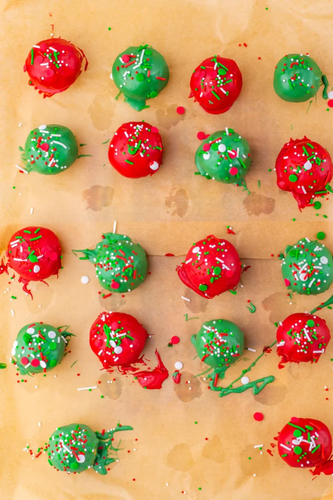 Christmas butterfinger balls coated in red and green chocolate with Christmas-themed sprinkles on top on parchment paper