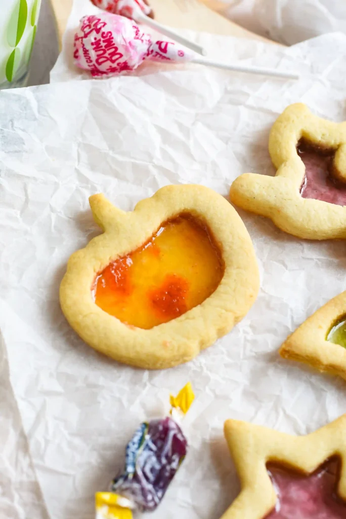 a stained glass sugar cookie of a pumpkin standing against a glass of milk