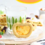 a stained glass sugar cookie of a pumpkin standing against a glass of milk
