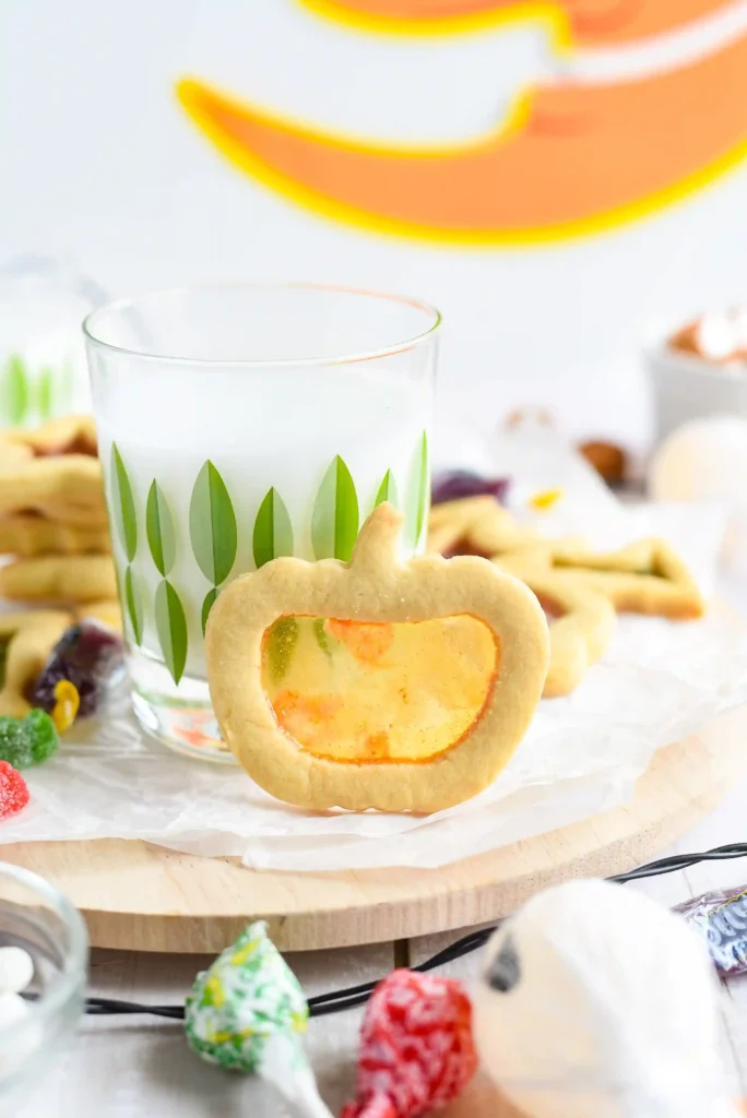 a stained glass sugar cookie of a pumpkin standing against a glass of milk