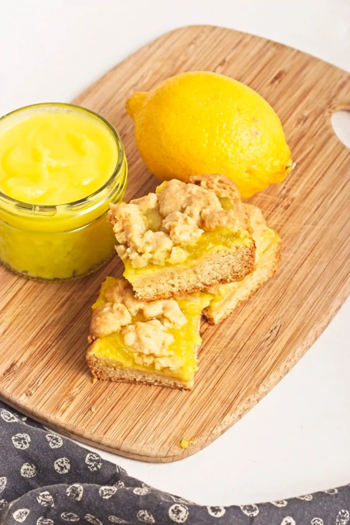 Lemon Curd Cookie Bars on a wooden board next to a jar of lemon curd