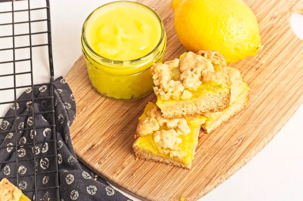 Lemon Curd Cookie Bars on a wooden board next to a jar of lemon curd