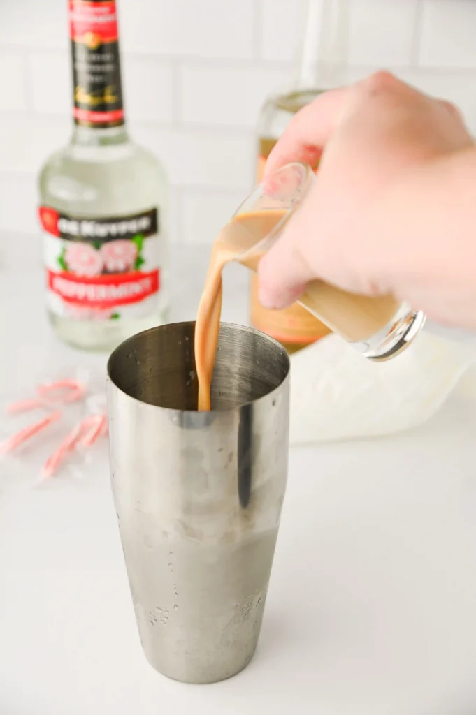 a hand pouring alcohol into a cocktail shaker