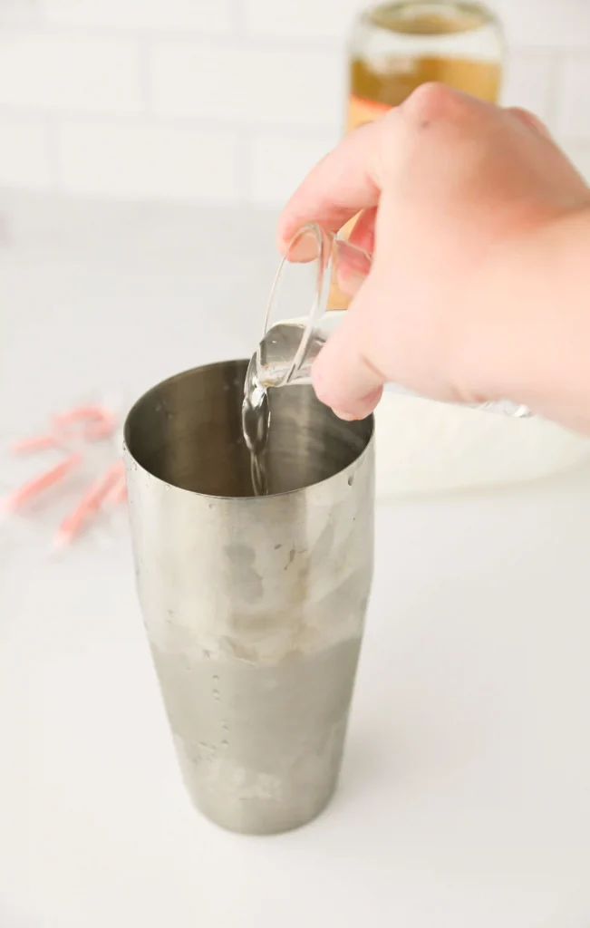 a hand pouring alcohol into a cocktail shaker