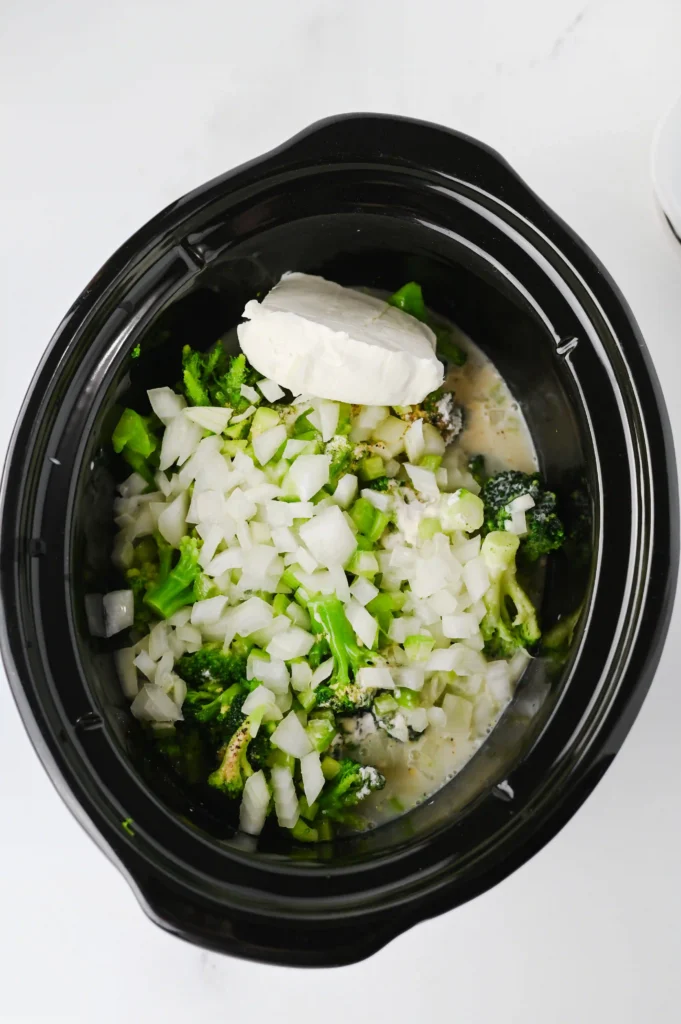 a crockpot filled with broccoli, spices, milk, and broth