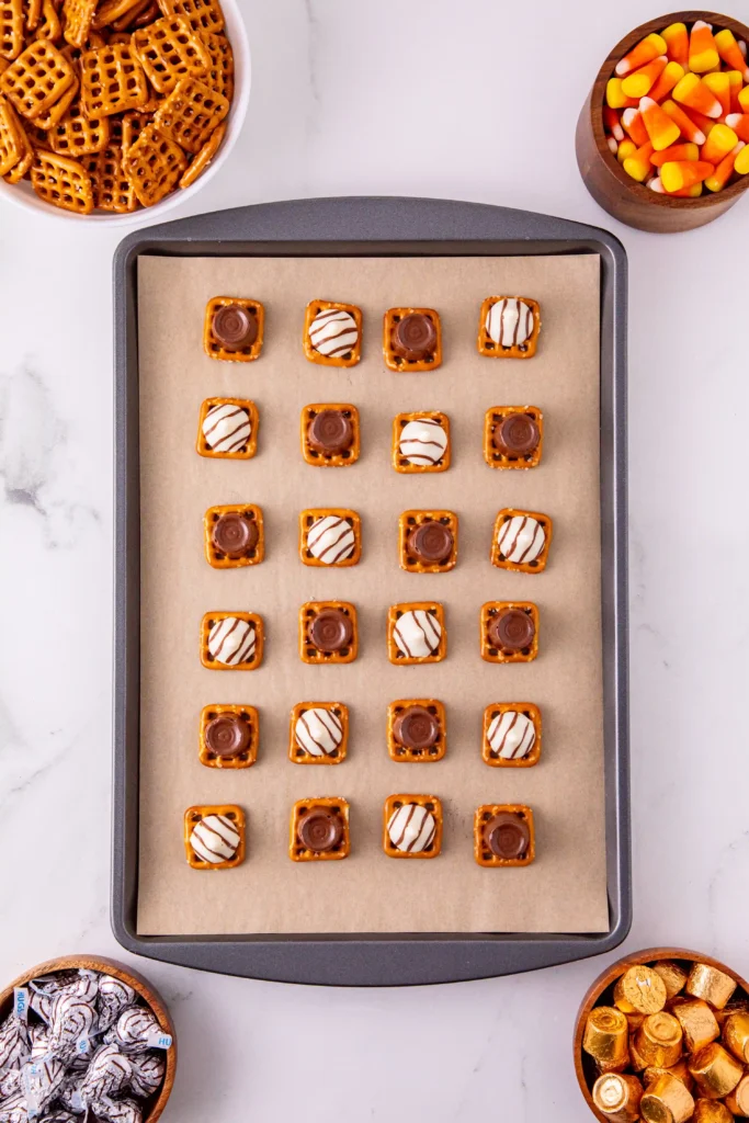 a baking sheet with parchment paper that has pretzel with rolls and Hershey kisses on top
