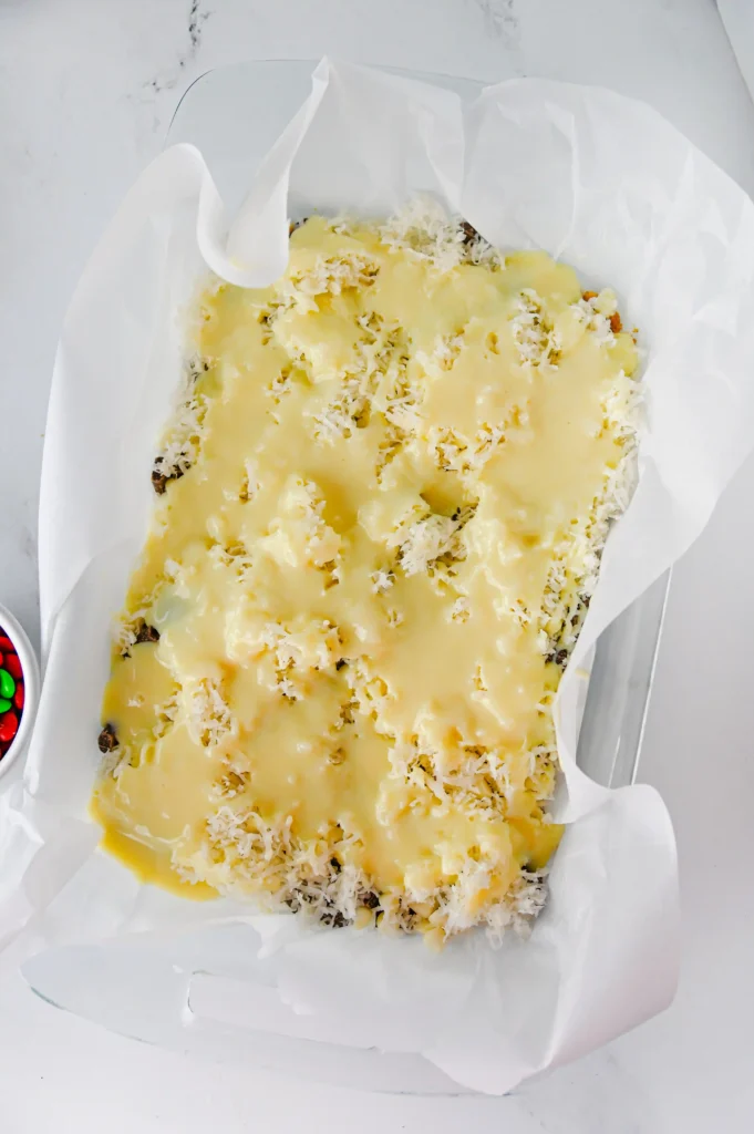 a graham cracker crust with pecans, chocolate chips, coconut and condensed milk on top