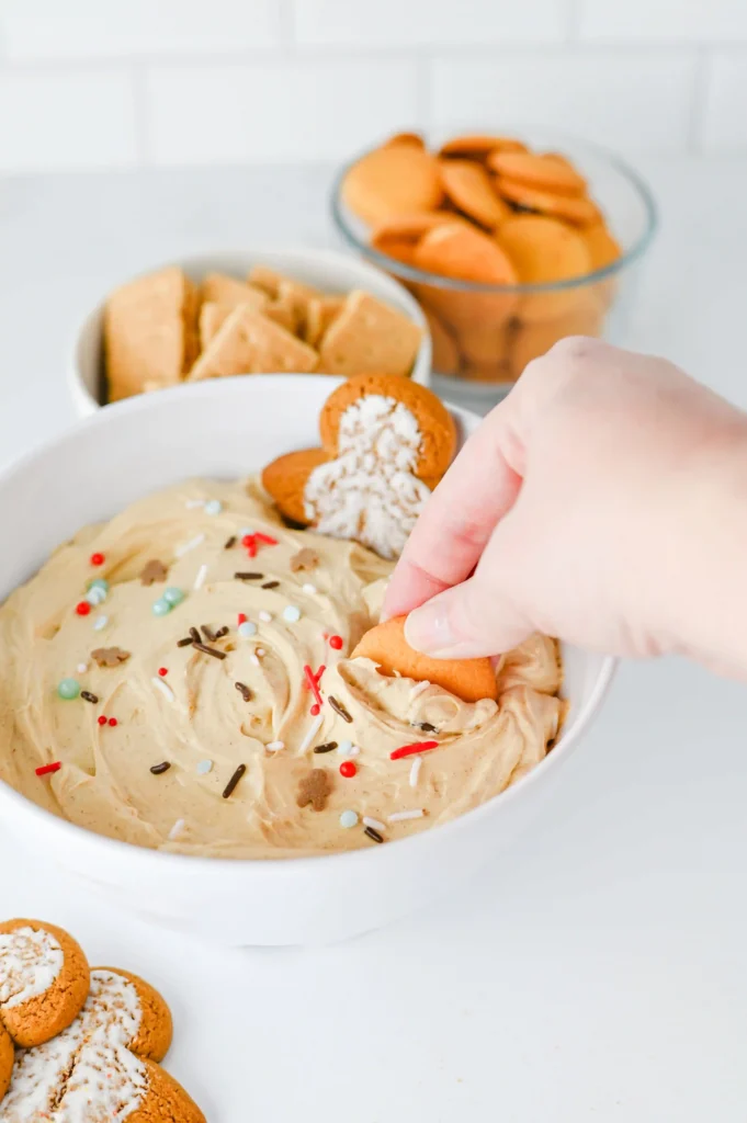 Gingerbread dip with sprinkles in a white bowl with a gingerbread cookie in it