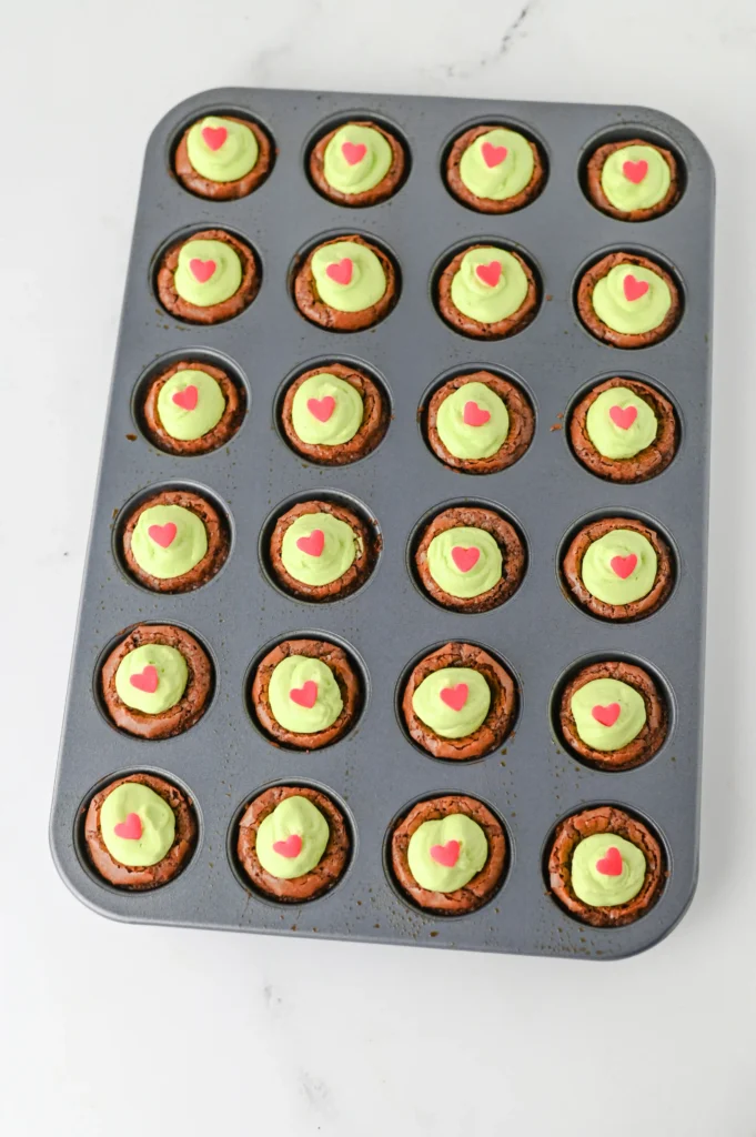 brownie bites with green frosting a heart sprinkles in a muffin tin