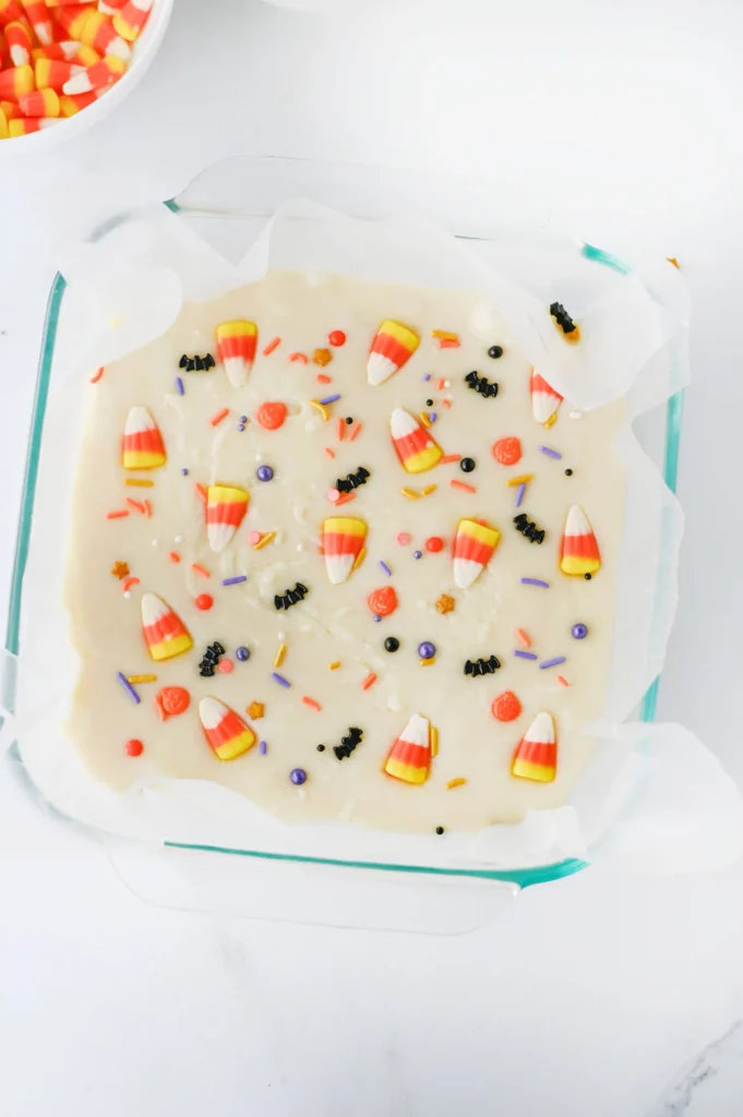 white chocolate fudge with candy corn and halloween sprinkles in a baking dish with parchment