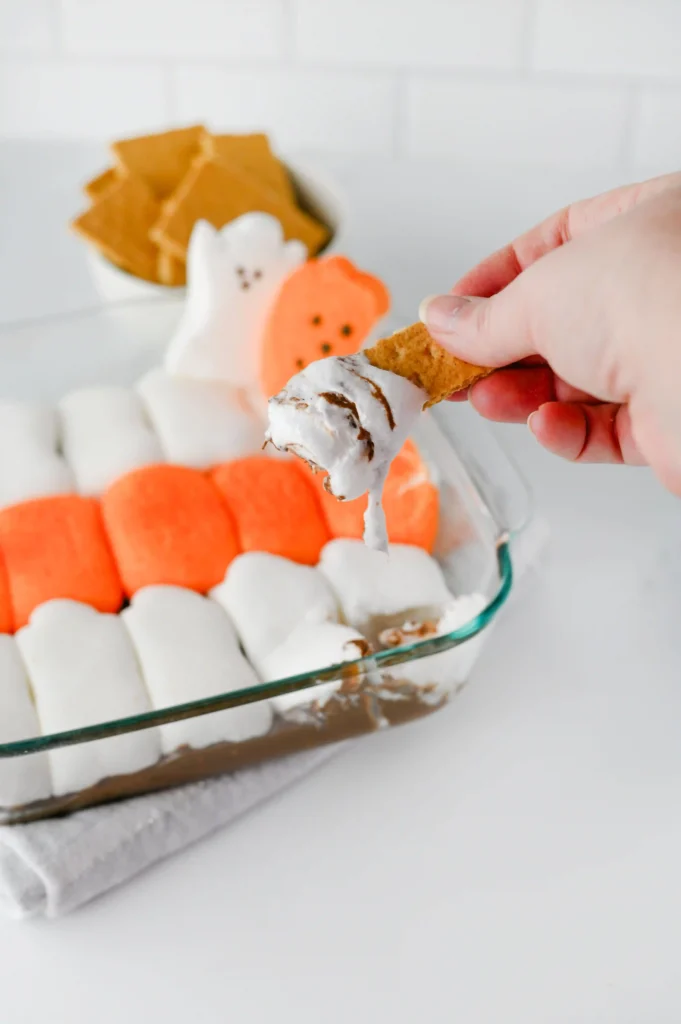 a hand dipping a graham cracker into the s'mores dip