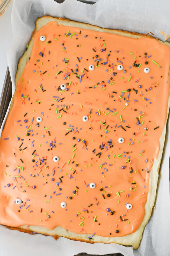 sugar cookie bars on a baking sheet with orange icing and halloween sprinkles