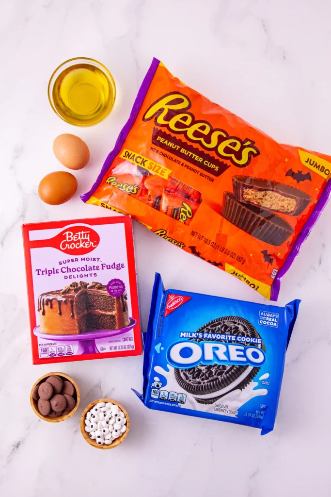 ingredients for the reese's oreo bat cookies: cake mix, oreos, reese's, eggs, oil, candy eyes, and chocolate
