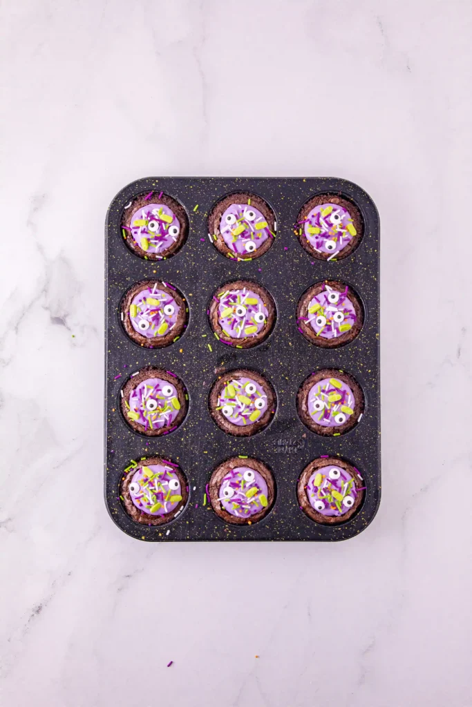 brownies with purple icing and halloween sprinkles in a muffin tin