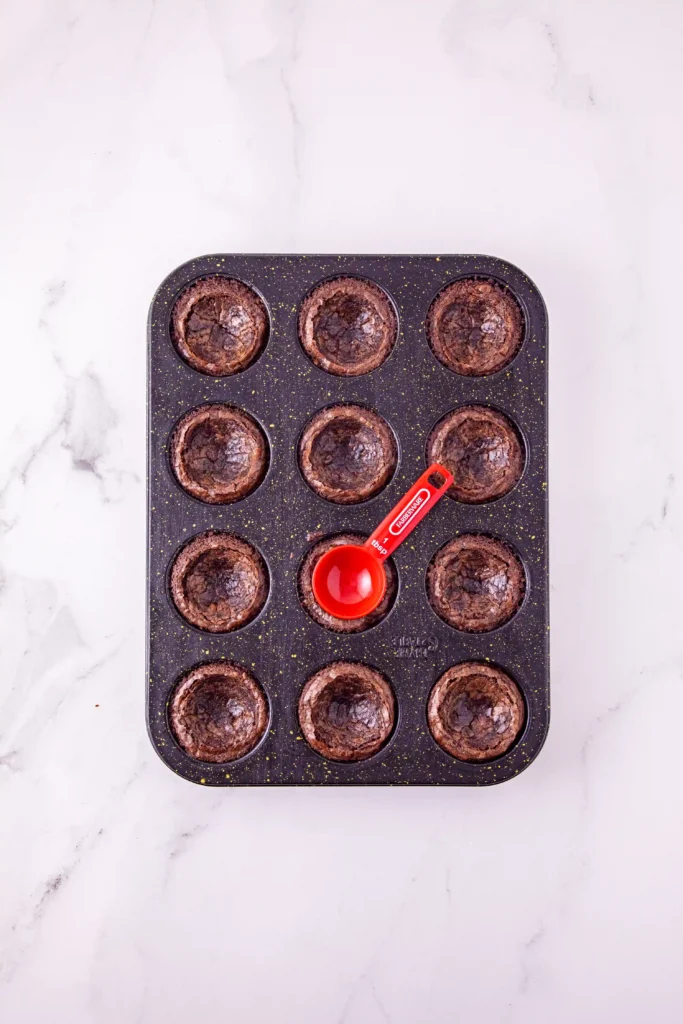 a muffin tin of baked brownies that have been pushed down with the measuring cup