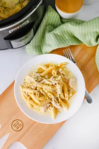 chicken Alfredo on a white plate next to a fork on a wooden board