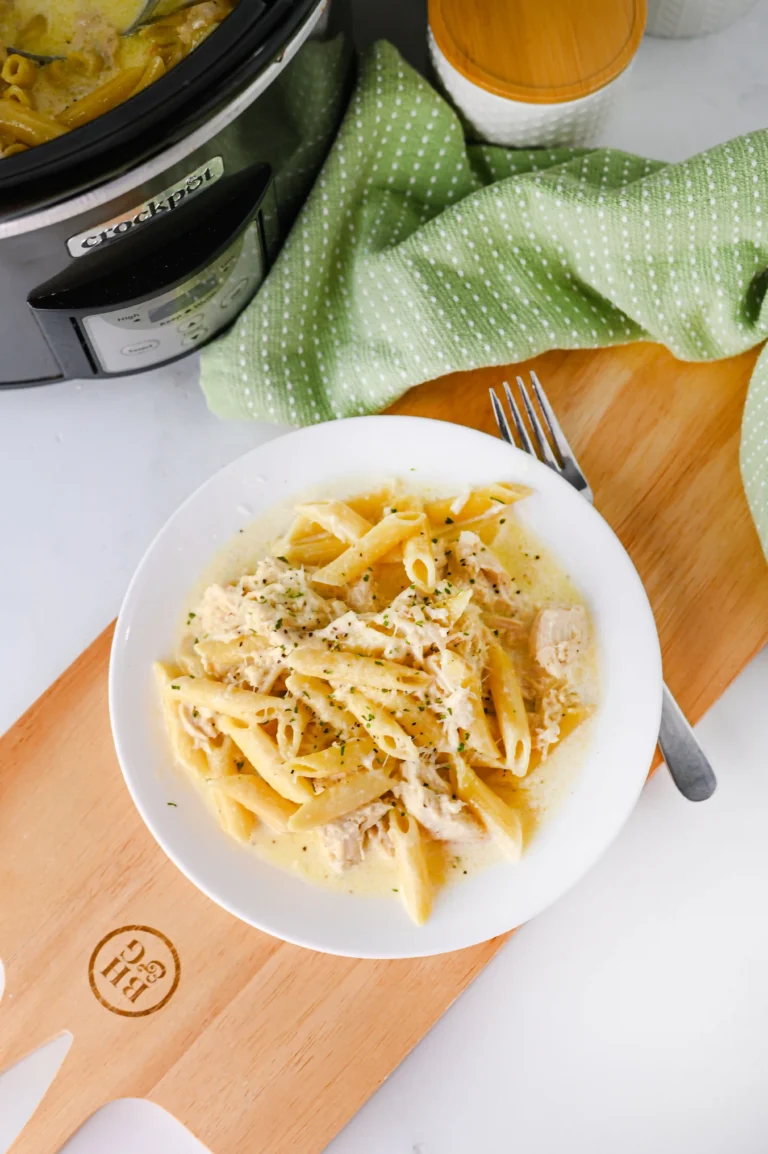 chicken Alfredo on a white plate next to a fork on a wooden board