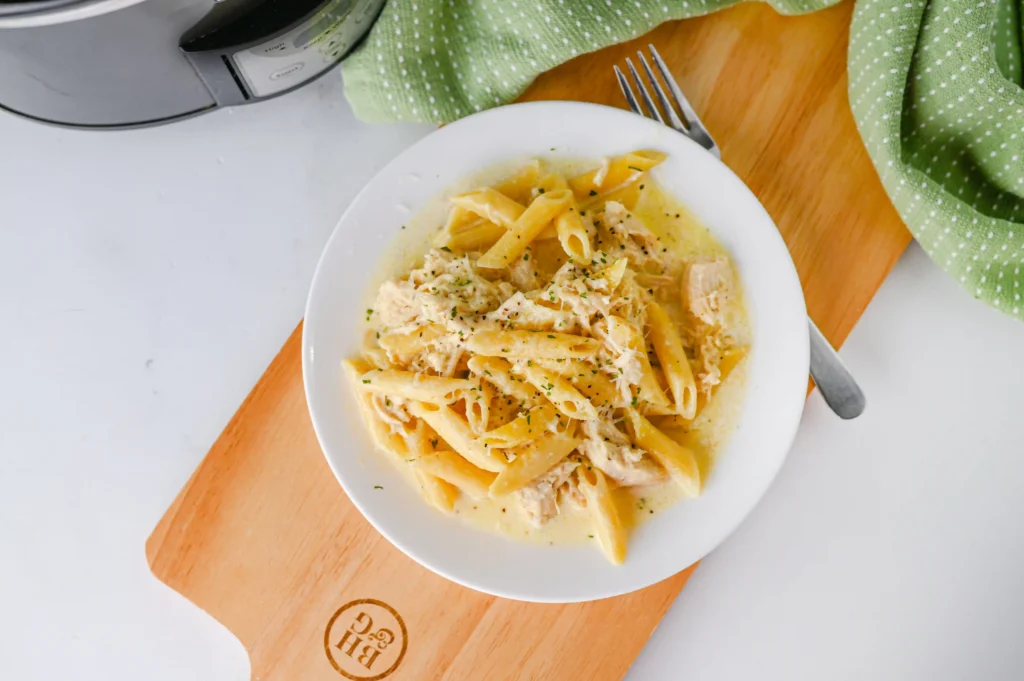 chicken Alfredo on a white plate next to a fork on a wooden board