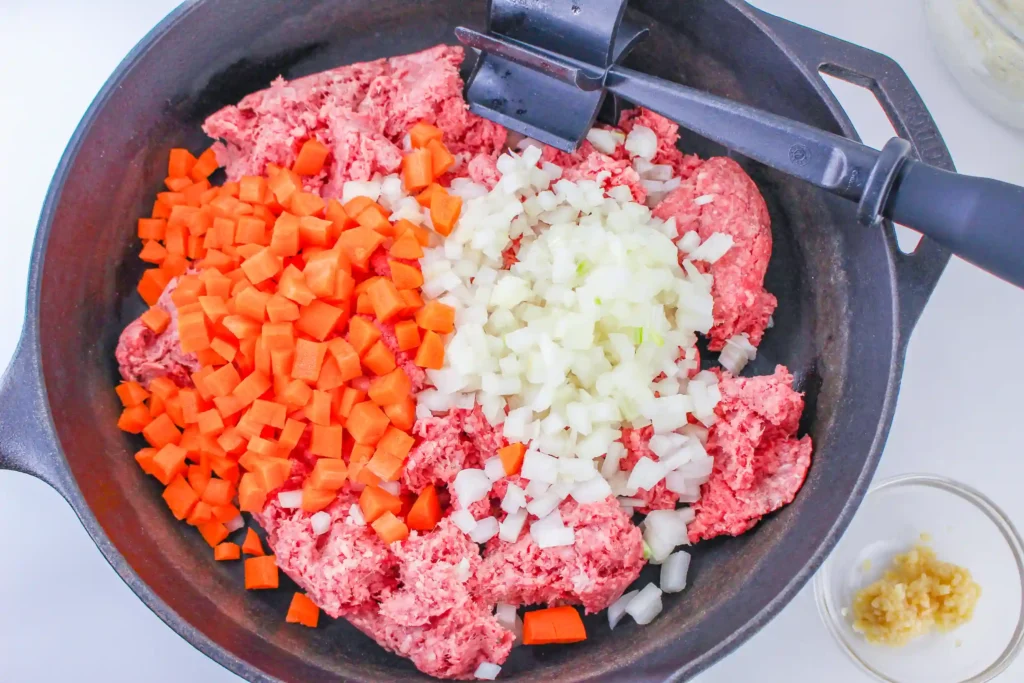 meat, onion, and tomatoes cooking in a pan