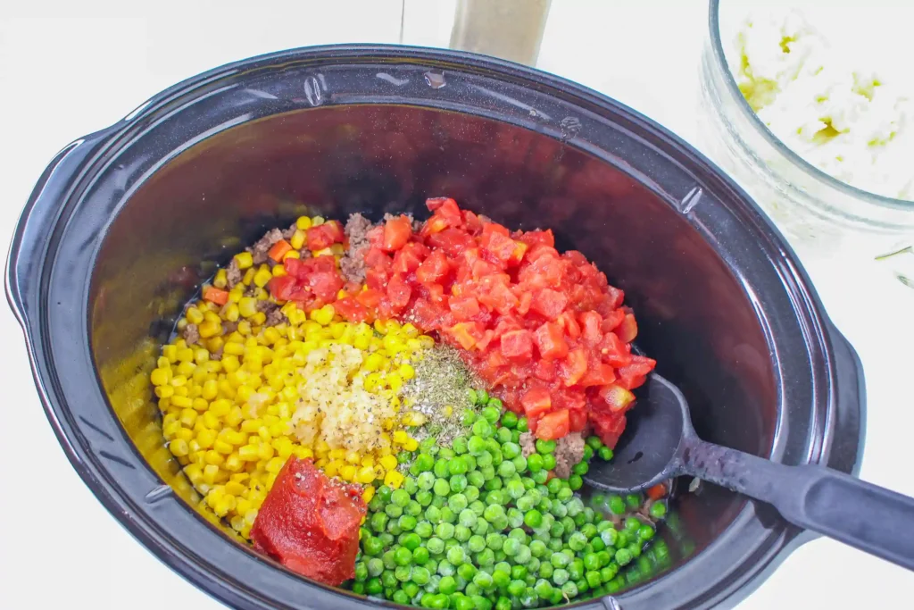 a crockpot with peas, corn, diced tomatoes, beef broth, tomato paste, Worcestershire sauce, dried thyme, salt, and pepper