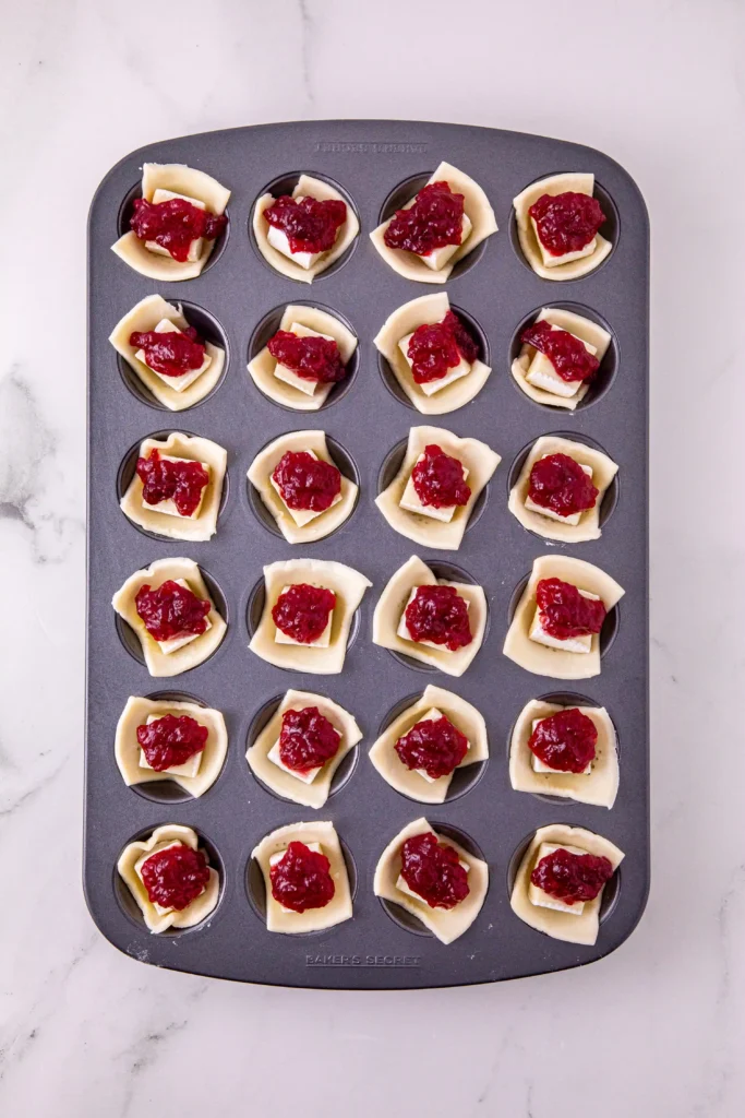 puff pastry squares in a muffin tin topped with brie cheese and cranberry sauce
