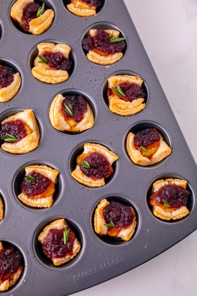 puff pastry squares in a muffin tin topped with brie cheese and cranberry sauce