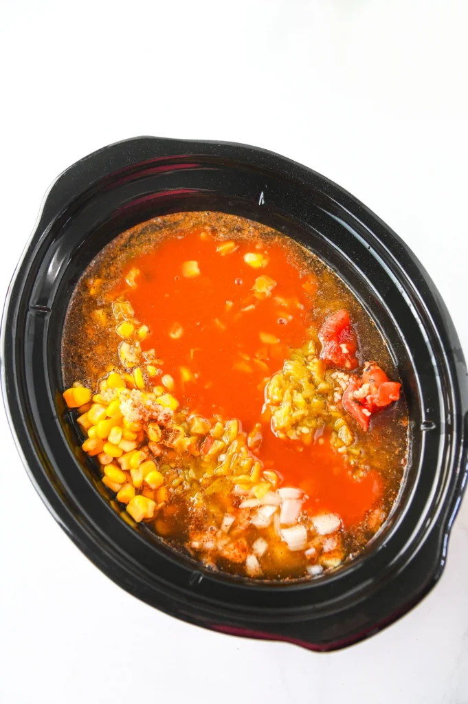 a crockpot with chicken broth, tomatoes, beans, corn, and chicken